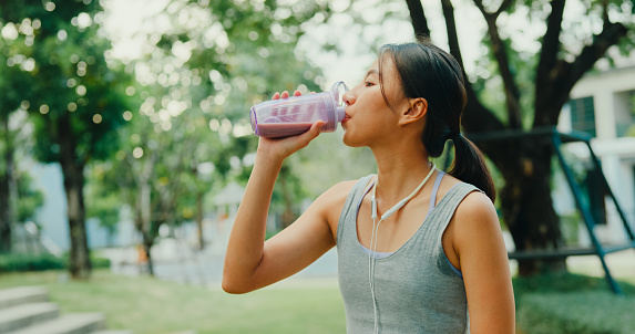 Young Asian female athlete runner drinking protein shake after exercise workout in urban park. Diet and healthy food workout exercise concept.