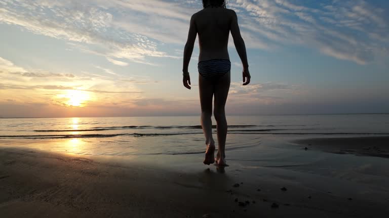 Barefoot child walks along the sandy seashore at sunset.