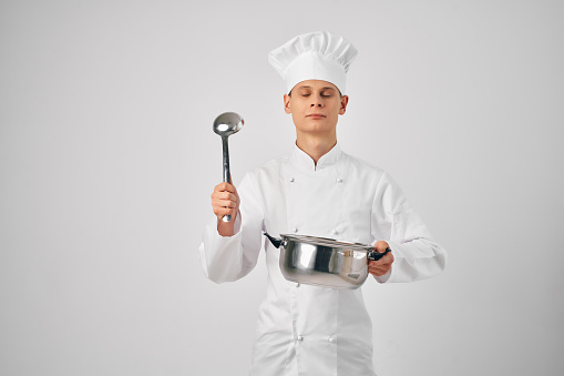 man in chef's clothes with a saucepan in his hands preparing food light background. High quality photo