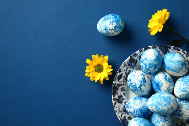 istock Plate with blue and white Easter eggs and yellow flowers on dark blue table. Top view. 2078818856