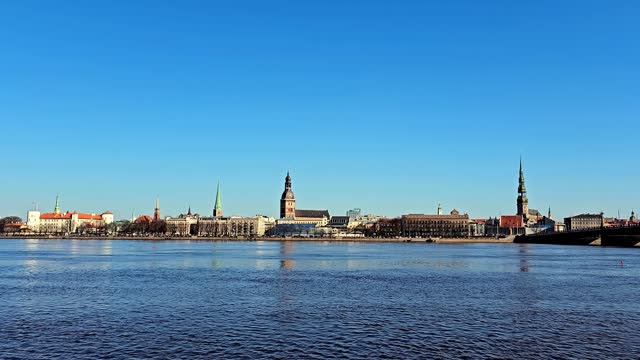 A wide shot of a city skyline across a calm river Daugava, with a city Riga bridge in the foreground