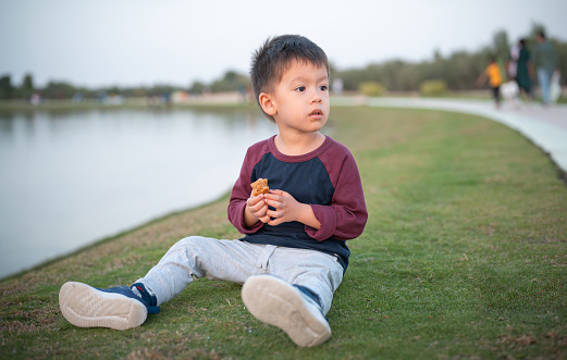 A young boy sits quietly on the grass, looking off to the side with a thoughtful expression, in a natural setting