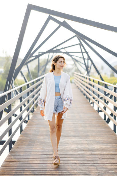 A woman is walking across a bridge, surrounded by a cityscape with buildings in the background.