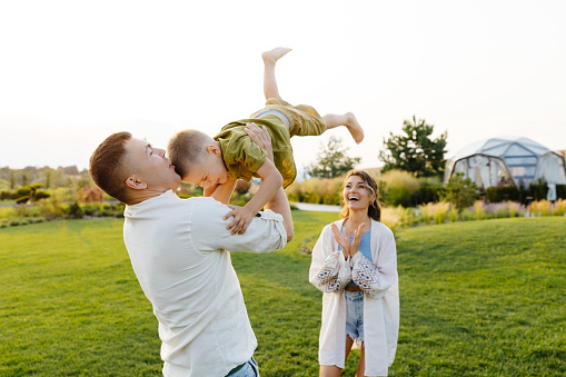 A man is lifting a young boy into the air with his arms extended upwards. The boy is smiling and appears joyful while being held above the ground.