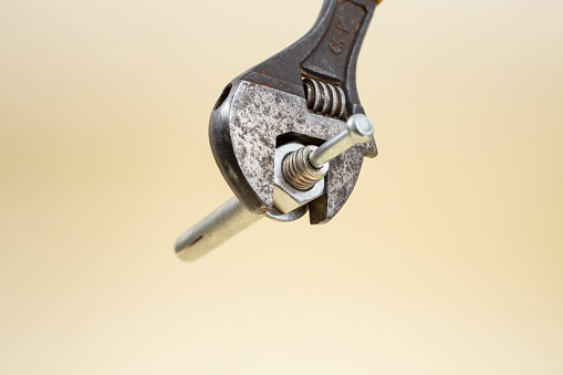 Adjustable wrench tightening a screw on beige background, soft focus