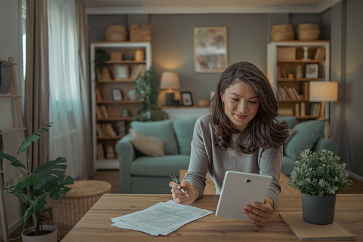 Photo of young woman sits at home , going through her finances and comparing them  using digital tablet