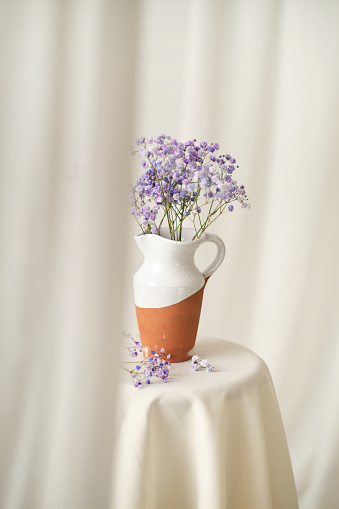 Vertical studio photo of still life of a curtain with jar with purple wild flowers