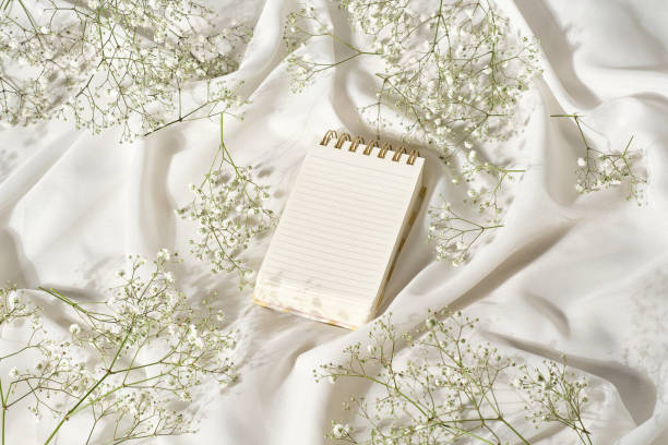 Mockup studio photo with a pocket notebook on a table with silk white cloth and flowers