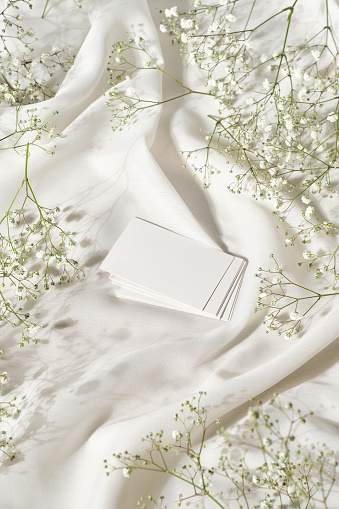 Mockup studio photo with elevated view of white blank card on a table with silk cloth and flowers