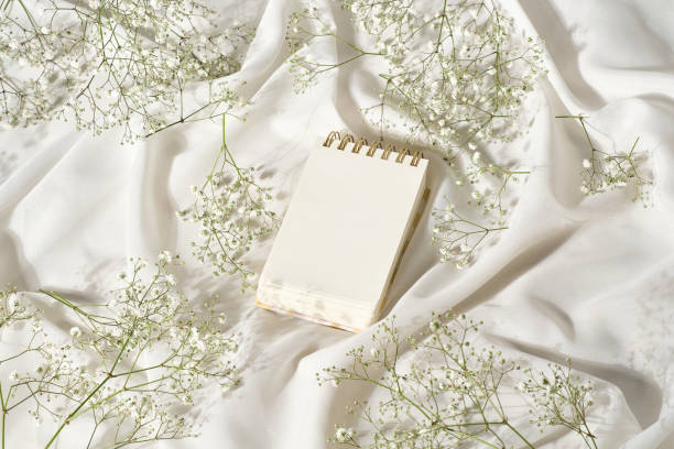Mockup studio photo with elevated view of a notebook on a table with soft textured silk cloth with white small flowers