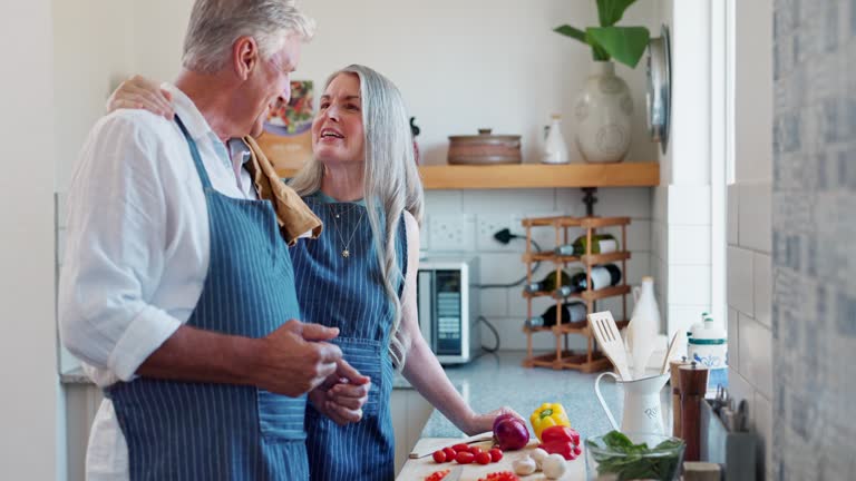 Old couple, cooking and vegetables in kitchen or together for healthy eating or dinner, bonding or nutrition. Man, woman and raw ingredients on board with conversation for wellness, meal prep or diet