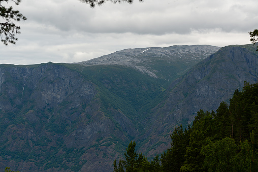 Nature view of Norwegian mountains with white snow cover on its high ground from stegastein viewpoint on a cloudy summer day. Blue uv radiation on the mountains.
