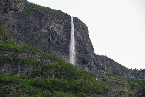 Norwegian fjord mountain nature view with waterfall and green trees growing at the foot of the mountain.
