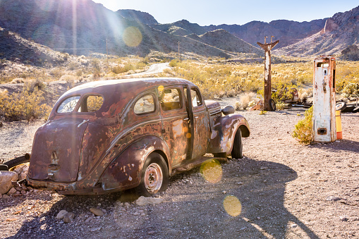 Old abandoned car and gas station off deserted road at sunset in the American Southwest with lens flare