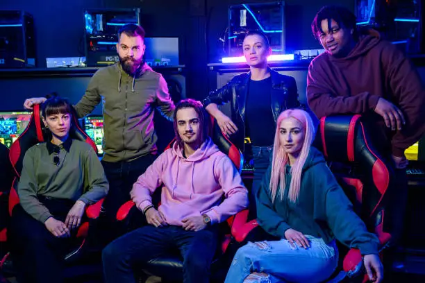 Portrait of a diverse team of gamers posing while looking at the camera in gameroom illuminated with a neon lights. Multiracial teammates participating on a cyber esport games tournament.
