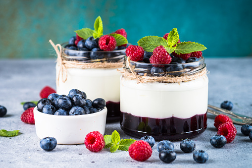 Parfait with cream or yogurt, jam and fresh berries in the glass jar. Close up. Healthy dessert or snack.