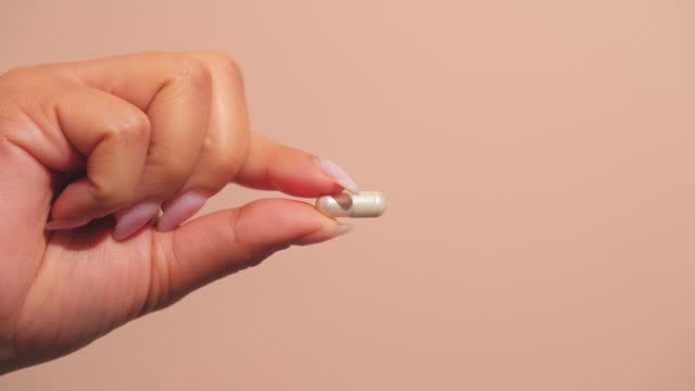 Female hand holds a capsule or pill, symbolizing wellness. Ideal for medical presentations or pharmaceutical ads.