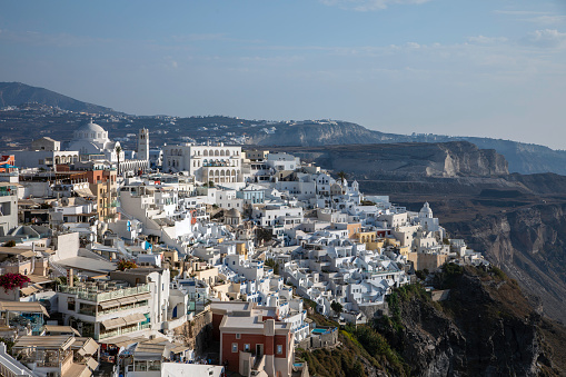 A beautiful view of the rugged cliff coastline near the town of Fira with little white and colourful houses, hotels, bars and famous blue domes churches on a sunny summer day. Firá is the modern capital of the Greek Aegean island of Santorini Thera one of the most beautiful holiday destinations in the world.