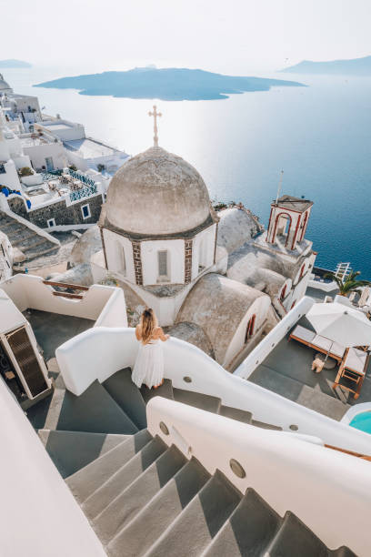 Young woman enjoys travelling and looking at views in Santorini, Greece Young beautiful woman tourist lady enjoys in white dress looking at the view of famous domes church ant city view panorama travel Greece vacation luxury Europe cruise destination of Thera, Greek Santorini island santorin stock pictures, royalty-free photos & images
