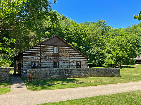 Mitchell, Indiana, USA - June 20, 2022:  Historic Lower Residence in the recreated and restored 1800 Pioneer Village at Spring Mill State Park, near Mitchell, Indiana with beautiful blue sky copy space and vivid green trees and grass.