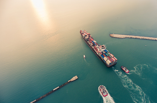 Aerial view of cargo ship leaving port with two tugboats.