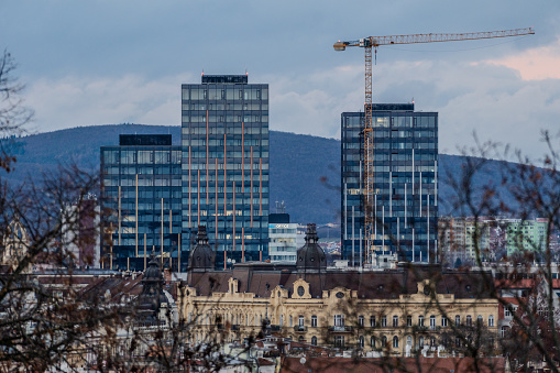 Brno, Czech Republic - 21 December 2023: Modern glass high-rise buildings in the historic city center with a tall crane. Architecture in the evening city.