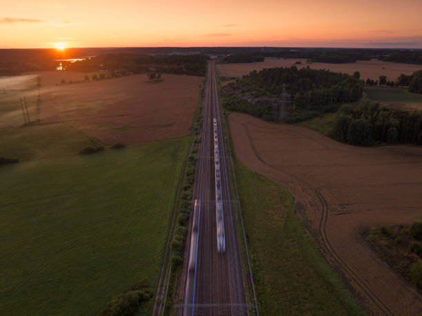 Two trains in blurred motion on a railway through a rural landscape at sunset in Uppland, Sweden.