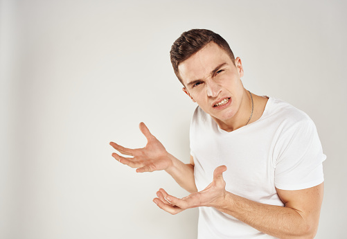A guy in a white T-shirt emotions irritability light background inadequate state. High quality photo
