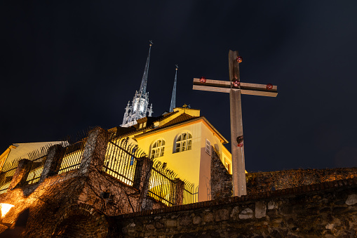 Brno, Czech Republic - 21 December 2023: A church with tall towers and a large wooden cross on the city walls at night in the city.