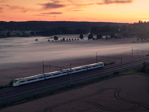 A train on a railway through a rural landscape on a misty evening in Uppland, Sweden.