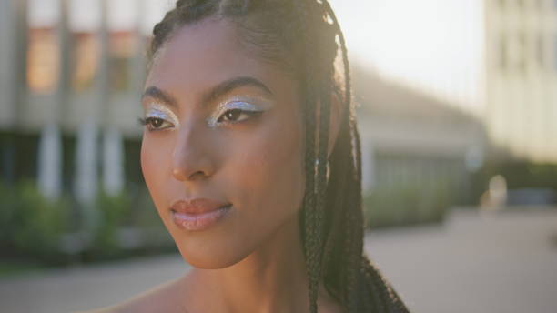 Dreadlocks lady looking camera at evening street portrait. Gorgeous brunette relaxing alone posing at sundown downtown. African american model woman with creative futuristic makeup at urban square