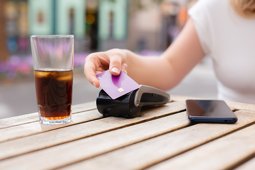 A woman is paying for a drink with a credit card at a table. A cell phone is on the table next to the credit card reader