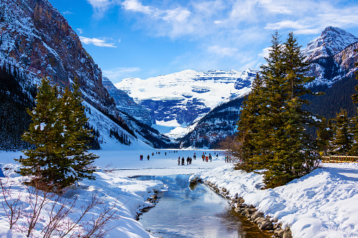 Frozen Lake Louise in the winter against the backdrop of the stunning Victoria Glacier. The iconic Lake Louise typically freezes from November to mid-April and draws visitors from all over the world during Winter.