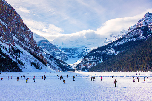 Unidentifiable visitors skating on frozen Lake Louise in the winter against the backdrop of the stunning Victoria Glacier. The iconic Lake Louise typically freezes from November to mid-April and draws visitors from all over the world during Winter.