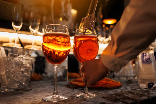 Bartender makes two glasses of cocktail Spritz on bar counter, adds fresh orange slices. Typical alcoholic Italian beverage, aperitif made with Prosecco sparkling white wine and ice cubes. Bartender makes two glasses of cocktail Spritz on bar counter, adds fresh orange slices. Typical alcoholic Italian beverage, aperitif made with Prosecco sparkling white wine and ice cubes crystal chalice stock pictures, royalty-free photos & images