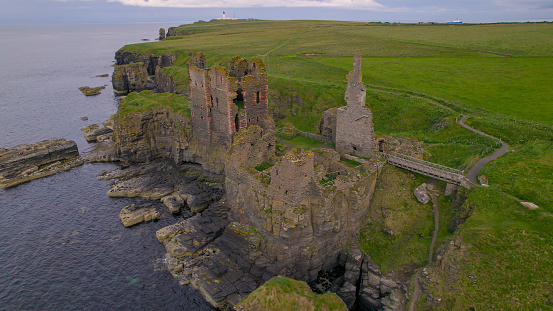 AERIAL: The ancient cliff top ruins of Sinclair Girnigoe Castle on a cloudy day. Scenic view of preserved remains of majestic historic stone fortress on the picturesque coast of northern Scotland.
