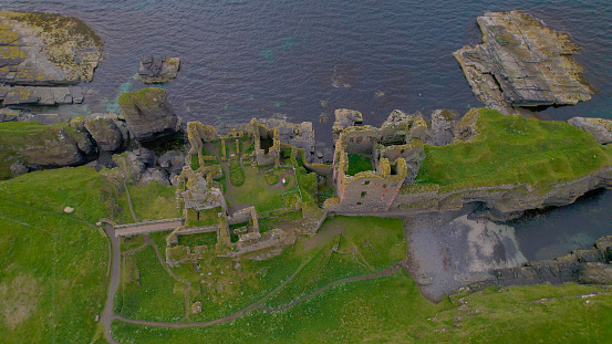 AERIAL TOP DOWN: Beautifully visible floor plan of remains of an ancient castle. Preserved ruins of a magnificent fortress atop a grassy cliff along the picturesque coast of Scotland on a cloudy day.