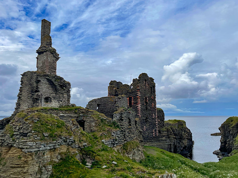 Old remains of medieval Castle Sinclair Girnigoe at the edge of grassy cliff. Incredible landscape shaped by ocean with stone ruins of an old fortress. Dramatic coast of Scotland steeped with history.