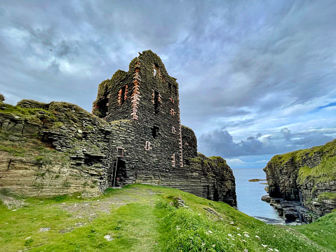 Stone ruins of a medieval Castle Sinclair Girnigoe on the edge of a grassy cliff. Amazing landscape shaped by ocean with remains of medieval fortress. Dramatic coast of Scotland steeped with history.