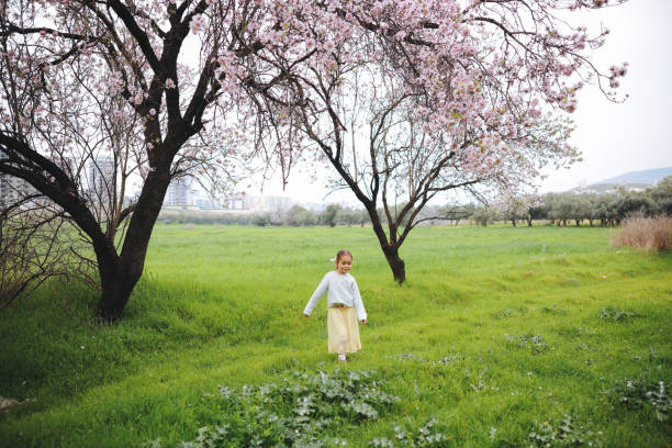Little girl taking a walk all alone in a park or forest. Cute girl running on the road in the park on a sunny day. Family time. Blooming trees