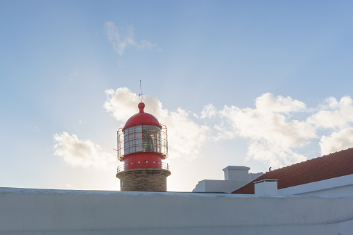 Tower of the lighthouse at Cabo de Sao Vicente with blue cloudy sky and sun shines from behind with light beams, Sagres, Algarve, Portugal