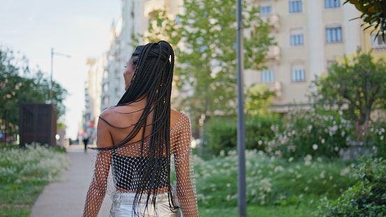 Afro braids girl walking green alley. Trendy african american lady turning camera enjoying summer portrait. Brunette in stylish outfit posing joyfully showing happy emotions. People lifestyle concept