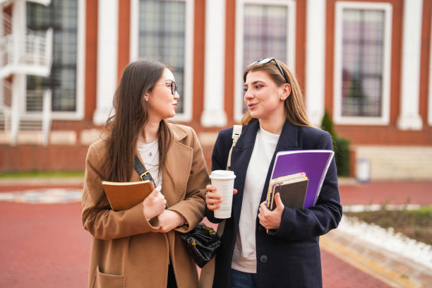Two female students go to class with books in their hands on the university campus