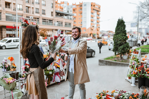 Female Florist Helping Smiling Male Choose A Beautiful Rose For His Wife On International Women's Day