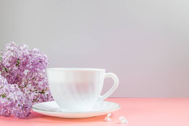 Cup of coffee and lilac flowers on light background.