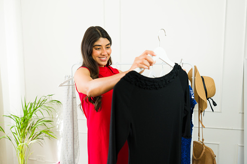 Cheerful young woman selecting clothes from a rack in a bright room