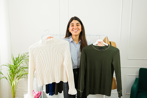 Smiling young female shopper choosing between two sweaters indoors