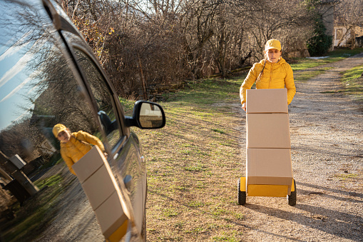 View of parked delivery van with female courier in uniform loading parcels for delivery.