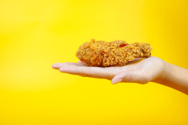 istock Female hand holding fried chicken on yellow background. 2079462736