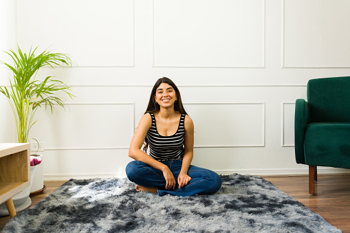 Smiling Hispanic woman sitting cross-legged on a rug in a bright living room